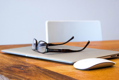 closed laptop with glasses resting on top of it all on a wooden table
