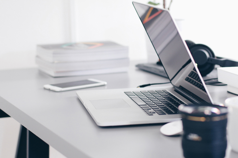 photo of a laptop, cell phone, coffee mug and a stack of books